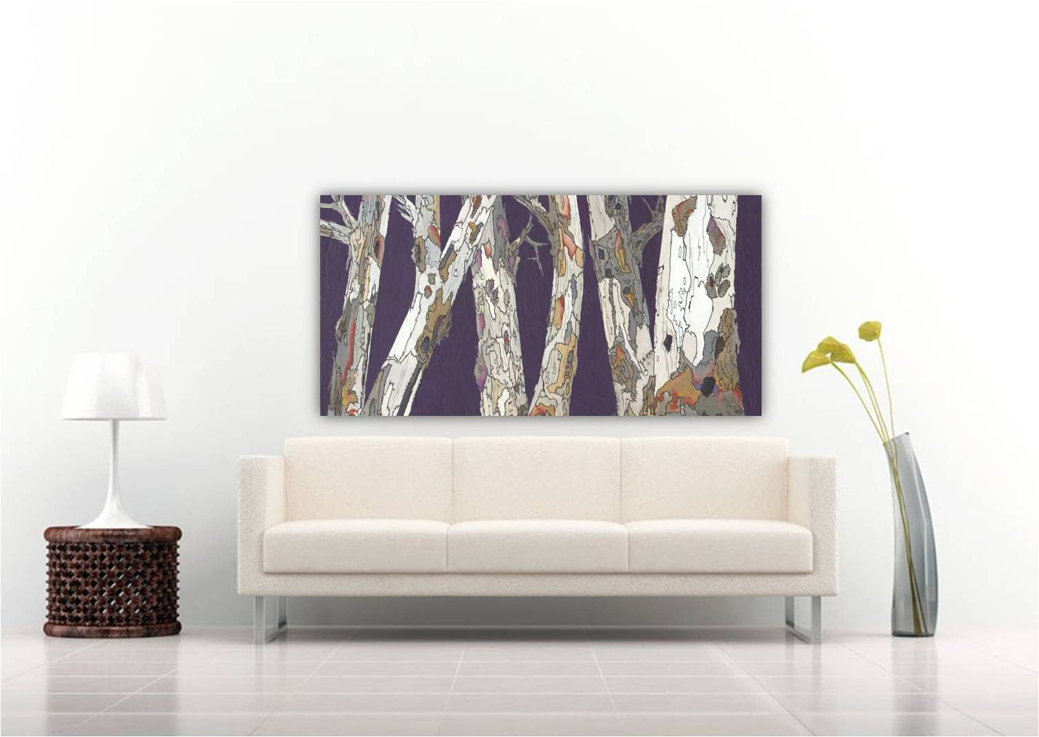 An extra large canvas wall art print featuring a modern purple and gray birch tree landscape, displayed above a white sofa in a clean, contemporary living room setting.