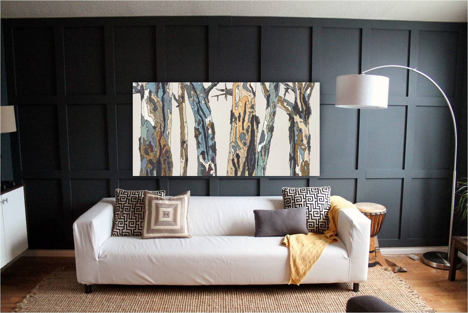 Very large artwork of trees in a landscape hung horizontally on a very dark wall above a sofa in an eclectic setting.