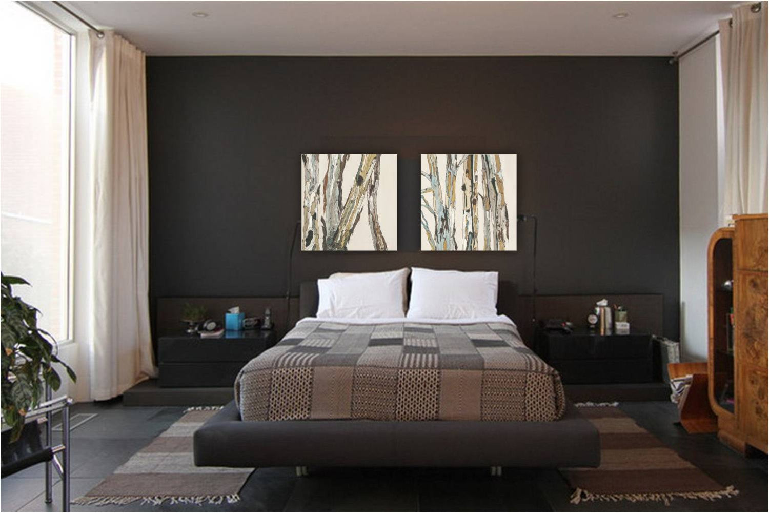 A set of two light colored canvas prints of trees on a dark wall above a masculine bedroom